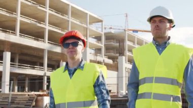 İnşaat alanının önünde duran profesyonel inşaatçılar. Ustabaşı ve inşaat mühendisi. Ofis binası ve vinç arka planı. İş, gayrimenkul ve yatırım kavramları.