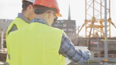 İnşaat alanının önünde duran profesyonel inşaatçılar. Ustabaşı ve inşaat mühendisi. Ofis binası ve vinç arka planı. İş, gayrimenkul ve yatırım kavramları.