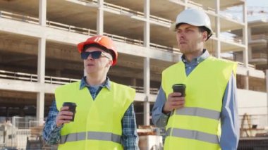 İnşaat alanının önünde duran profesyonel inşaatçılar. Ustabaşı ve inşaat mühendisi. Ofis binası ve vinç arka planı. İş, gayrimenkul ve yatırım kavramları.