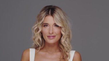 Gri arka planda genç, güzel ve anlamlı sarışın bir kadının stüdyo portresi..