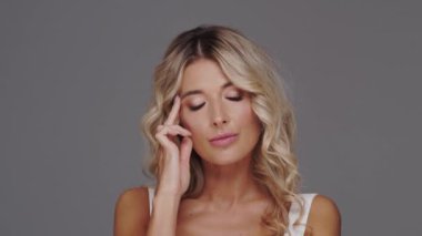 Gri arka planda genç, güzel ve anlamlı sarışın bir kadının stüdyo portresi..