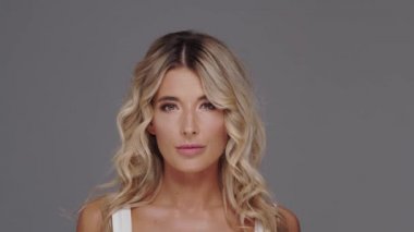 Gri arka planda genç, güzel ve anlamlı sarışın bir kadının stüdyo portresi..