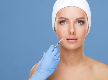 Genç bir kadının güzel yüzüne iğne yapan bir doktor. Estetik ameliyat, cilt gerdirme ve estetik tıp konsepti.
