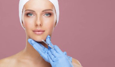 Genç bir kadının güzel yüzüne iğne yapan bir doktor. Estetik ameliyat, cilt gerdirme ve estetik tıp konsepti.