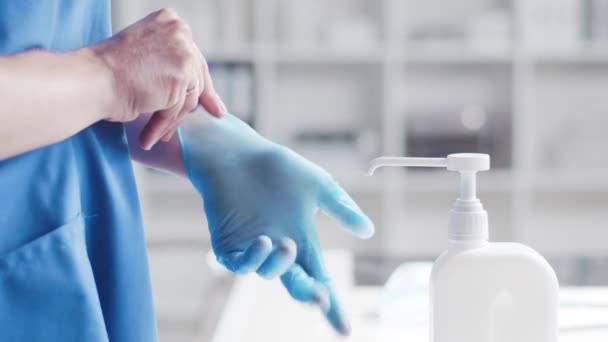 Zbliżenie lekarza zakładającego rękawiczki i czyszczącego ręce środkiem dezynfekującym z mydłem medycznym. Biuro w szpitalu na tle. — Wideo stockowe