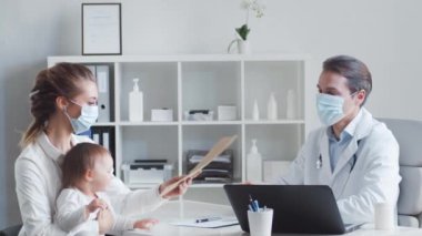 Erkek çocuk doktoru küçük hasta bebeği muayene ediyor. Doktor, anne ve kızı klinikteki muayenehanede. Sağlık hizmetleri kavramı.