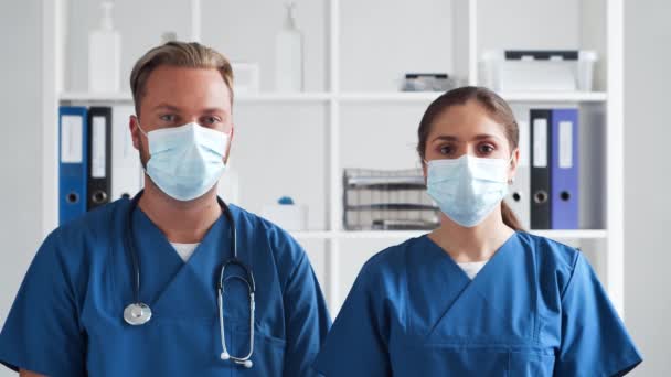 Kórházi rendelőben dolgozó hivatásos orvosok, fiatal és magabiztos orvosok portréja védőmaszkban. — Stock videók