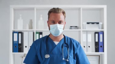 Hastane ofisinde profesyonel tıp doktoru koruyucu maskeli genç ve kendinden emin bir doktorun portresi..