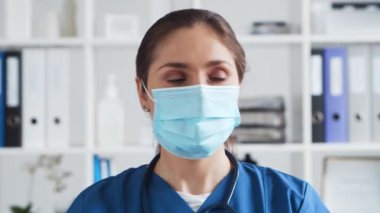 Hastane ofisinde profesyonel tıp doktoru koruyucu maskeli genç ve çekici bir kadın doktorun portresi..