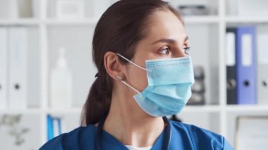 Hastane ofisinde profesyonel tıp doktoru koruyucu maskeli genç ve çekici bir kadın doktorun portresi..