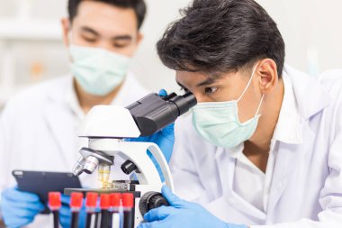 Biyolojik bilim laboratuvarlarında çalışan sağlık araştırmacıları, bir araştırmacı mikroskobik ve asistanı laboratuvarda virüsün bilgilerini analiz etmek için tablet bilgisayar kullanıyor.