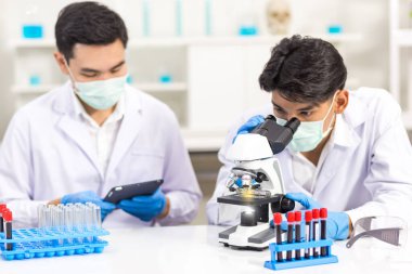 Biyolojik bilim laboratuvarlarında çalışan sağlık araştırmacıları, bir araştırmacı mikroskobik ve asistanı laboratuvarda virüsün bilgilerini analiz etmek için tablet bilgisayar kullanıyor.