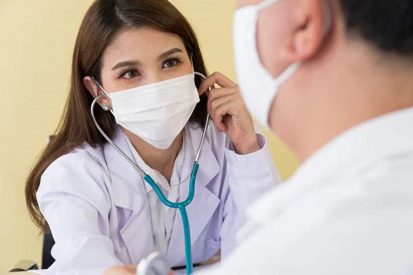 The female doctor wearing a surgical mask and using a stethoscope to check the pulse and look at a male patient, focus on the doctor.