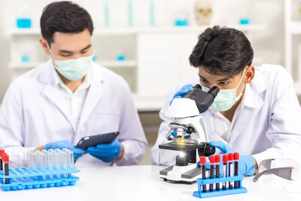 Biyolojik bilim laboratuvarlarında çalışan sağlık araştırmacıları, bir araştırmacı mikroskobik ve asistanı laboratuvarda virüsün bilgilerini analiz etmek için tablet bilgisayar kullanıyor.