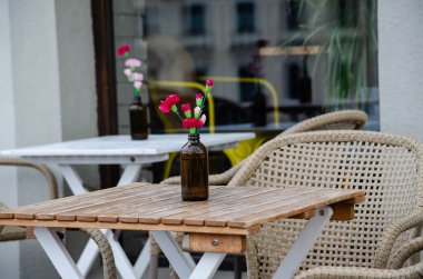 Ahşap masada kırmızı karanfilli cam bir vazo duruyor.