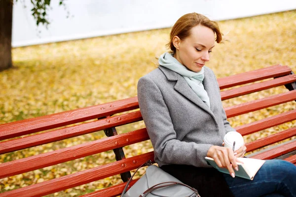 Young pretty woman sitting on a bench in autumn park — Stock Photo, Image