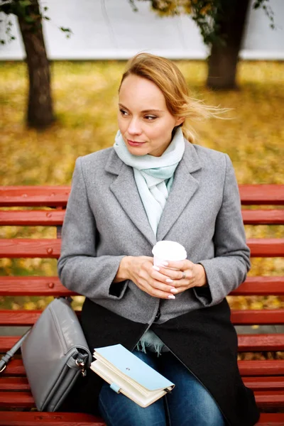 Pretty blonde woman sitting alone on a bench in autumn park — Stock Photo, Image