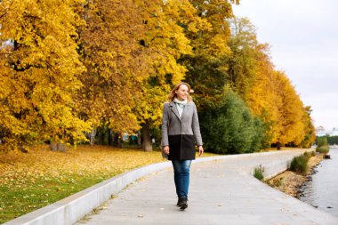 Şehir parkında nehir boyunca yürüyen zarif kendine güvenen kadın 