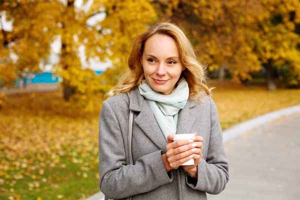 Sıcak bir fincan kahve tutan genç gülümseyen kadın