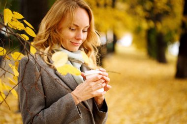 Güneşli sonbahar gününde kahve açık havada genç gülümseyen kadın