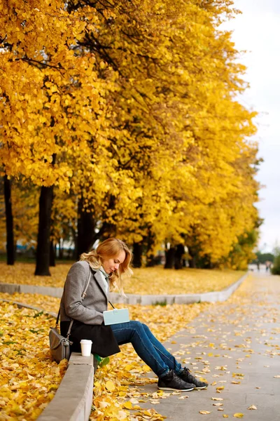 Woman sitting on a curb and writing something in her notebook — Stock Photo, Image