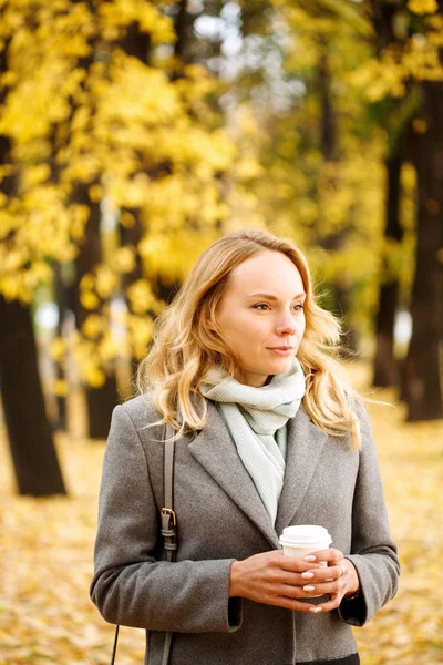 Jonge zelfverzekerde vrouw met koffie buitenshuis in zonnige herfst dag — Stockfoto