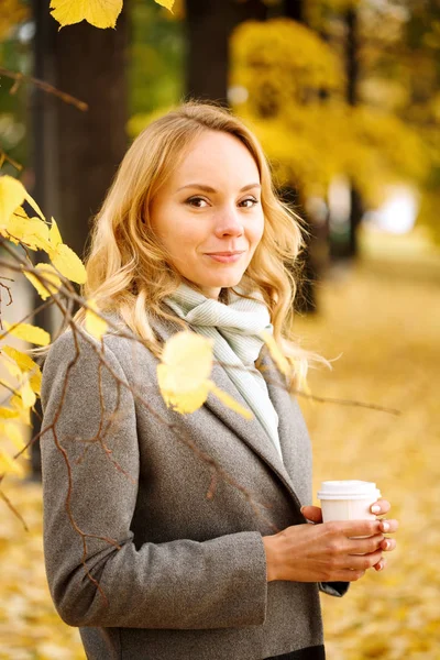 Młoda uśmiechnięta kobieta z kawą na świeżym powietrzu w słonecznym jesiennym dniu — Zdjęcie stockowe