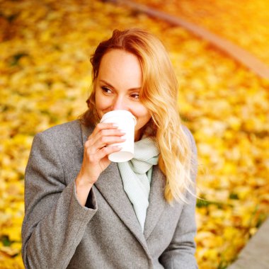 Sonbahar parkında kahve içen neşeli güzel kadın