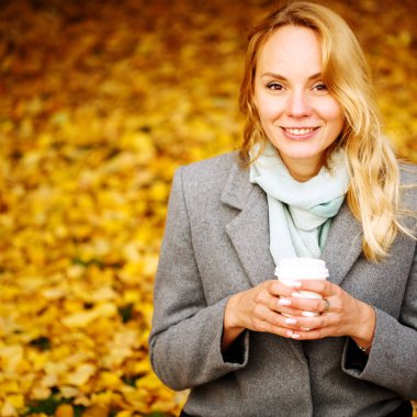 Sonbahar parkında kahve içen neşeli güzel kadın