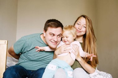 30 'lu yaşlardaki genç ebeveynler ellerinde tutuyorlar. Yüzünde komik bir ifade olan yaramaz küçük kız çocuğu.