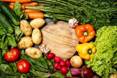 Ahşap kesim tahtasının etrafındaki taze sebzelerden yapılmış çerçeve: biber, patates, domates, turp, salata. 