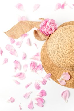 Yaz tatili konsepti, saman örgülü şapka, pembe şakayık çiçekleri ve beyaz arka planda taç yaprakları, üst manzara. Tatil ve seyahat afişi.