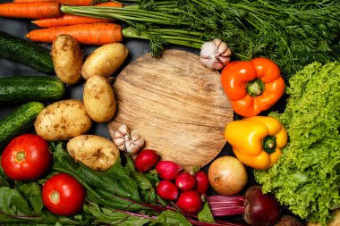 Ahşap kesme tahtasının etrafındaki taze sebzelerden yapılmış çerçeve.