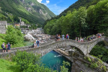 Lavertezzo, Switzerland - 9 June 2018: people walking over the Roman bridge at Lavertezzo on the Swiss alps clipart