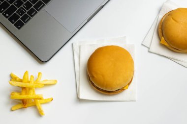 İş atıştırma adlı lokanta. Dizüstü bilgisayar, hamburger ve patates kızartması işyerinde. Meze beyaz masanın üzerinde.
