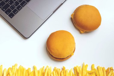İş atıştırma adlı lokanta. Dizüstü bilgisayar, hamburger ve patates kızartması işyerinde. Meze beyaz masanın üzerinde.