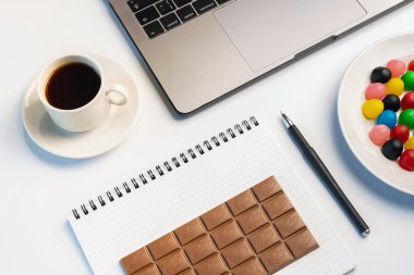 İş yerinde meze, bir ısırık kavram var. Dizüstü bilgisayar, şeker ve çalışma kitabıyla çikolata ve kahve işyerinde çubuğunda. Düz yatıyordu, en iyi görünüm, beyaz masa.