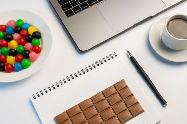 İş yerinde meze, bir ısırık kavram var. Dizüstü bilgisayar, şeker ve çalışma kitabıyla çikolata ve kahve işyerinde çubuğunda. Düz yatıyordu, en iyi görünüm, beyaz masa.