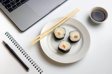 İş yerinde yemek suşi rulo. Mola zamanı suşi yemek için. Laptop ve defter beyaz organize masa üzerinde.