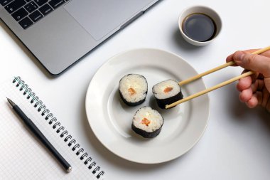 İş yerinde yemek suşi rulo. Mola zamanı suşi yemek için. Laptop ve defter beyaz organize masa üzerinde.