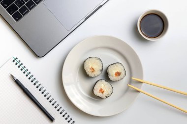 İş yerinde yemek suşi rulo. Mola zamanı suşi yemek için. Laptop ve defter beyaz organize masa üzerinde.