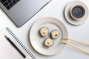 İş yerinde yemek suşi rulo. Mola zamanı suşi yemek için. Laptop ve defter beyaz organize masa üzerinde.