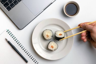 İş yerinde yemek suşi rulo. Mola zamanı suşi yemek için. Laptop ve defter beyaz organize masa üzerinde.