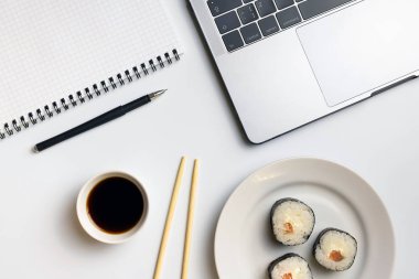 İş yerinde yemek suşi rulo. Mola zamanı suşi yemek için. Laptop ve defter beyaz organize masa üzerinde.