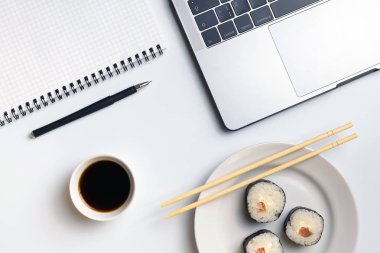 İş yerinde yemek suşi rulo. Mola zamanı suşi yemek için. Laptop ve defter beyaz organize masa üzerinde.