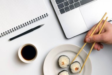 Mola zamanı suşi yemek için. İş yerinde yemek suşi rulo. Laptop ve defter beyaz organize masa üzerinde.