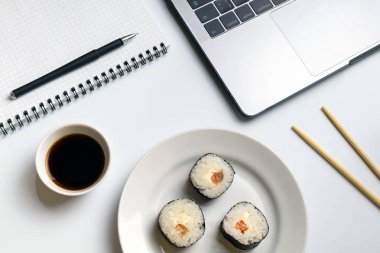 Mola zamanı suşi yemek için. İş yerinde yemek suşi rulo. Laptop ve defter beyaz organize masa üzerinde.