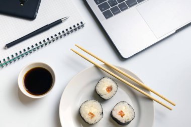 İş yerinde yemek suşi rulo. Mola zamanı soya sosu ile yemek suşi için. Dizüstü bilgisayar, dizüstü bilgisayar ve beyaz organize Resepsiyon üstünde hareket eden telefon.