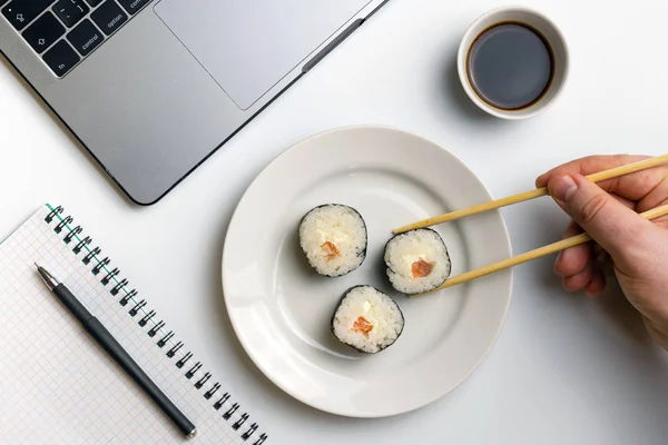Sushi rolls snacking at work. Break time for sushi eating. Laptop and notebook on white organized desk.