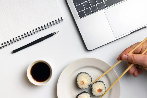 Break time for sushi eating. Sushi rolls snacking at work. Laptop and notebook on white organized desk.